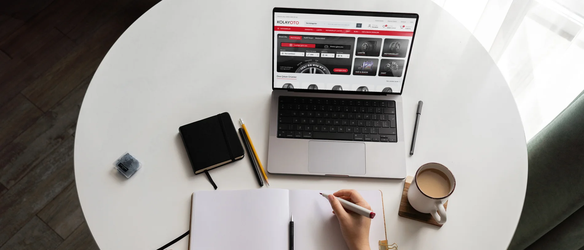 Yuvarlak beyaz masada ekranında Kolayoto web sitesi açık dizüstü bilgisayar, açık defter ve not alan el